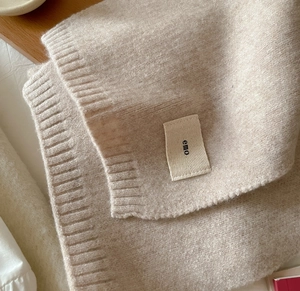Close-up of oatmeal knitted scarf texture with small lettered brand tag and soft knit pattern