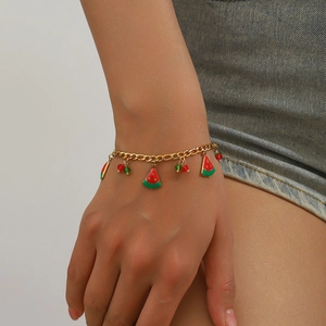 Bracelet à chaîne dorée avec breloques pastèque et cerise porté sur un poignet