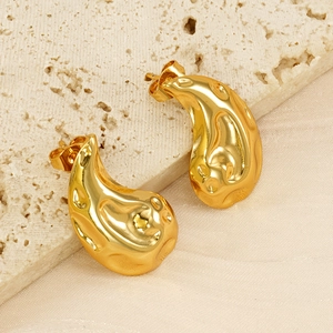Close-up of golden fluid teardrop earrings on a stone base with silk background