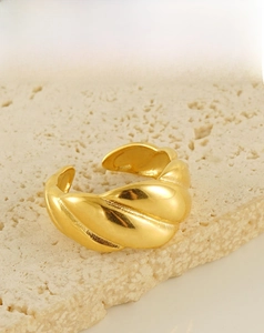 Detailed view of gold twisted croissant ring on beige stone background showing 18k texture