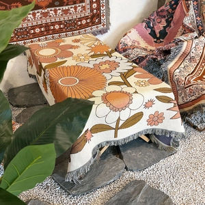 Detail of bohemian woven camping blanket featuring orange floral patterns and fringed edges