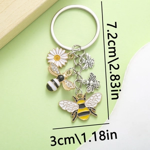 Bee and daisy enamel charm keychain with gold finish on a soft green background