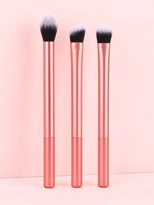 Gros plan de trois pinceaux de maquillage or rose avec poils synthétiques bicolores sur rose
