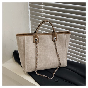 Detail view of large beige canvas tote bag with brown leather handles and chain strap