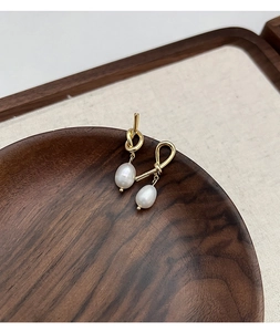 Detail of gold knotted earrings with natural freshwater pearls on a wooden tray