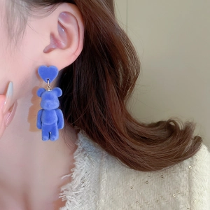 Detailed close-up of blue flocked heart and teddy bear earrings worn by a model