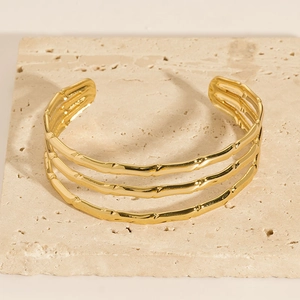 Close-up of golden 18K gold-plated triple bamboo joint C-shape open bangle on stone