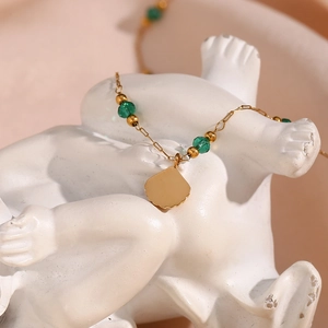 Golden titanium steel necklace featuring green beads and a shell pendant on a white bust
