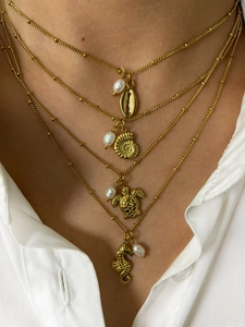 Detailed layered gold necklace with seahorse and turtle pendants with pearls on a model