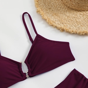 Close-up of wine red bikini with ruched fabric and metal ring hardware on white background