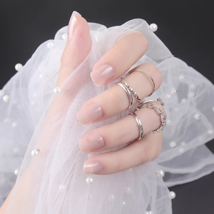 Close-up of glossy nude short square press-on nails with silver rings on pearl lace