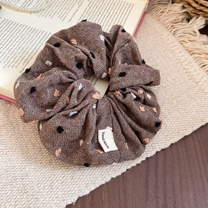 Detail of a brown textured scrunchie with colorful pompoms and Hand Made label on a book
