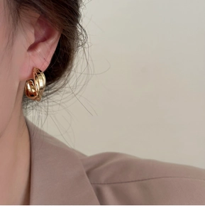 Gros plan d'un mannequin portant un ear cuff géométrique torsadé en métal doré poli