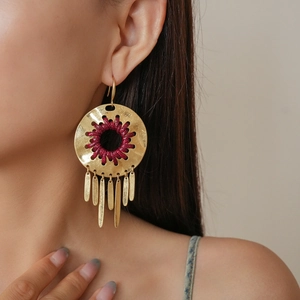 Detail of golden tassel earrings with burgundy woven center worn by a model