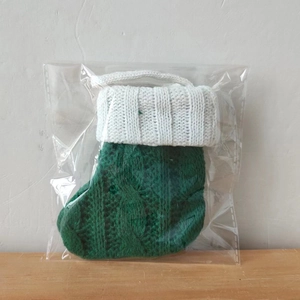 Close-up of a green knitted Christmas stocking silverware holder in clear packaging