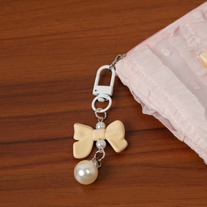 Detail of a beige bow keychain with white metal hook and elegant pearl pendant charms