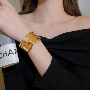 Detailed view of wide irregular wrinkled golden stainless steel cuff bracelet on model wrist