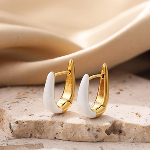 Macro shot of U-shaped earrings in gold finish and white enamel on silk background