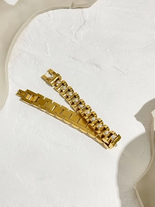Detail of 18K gold watchband link bracelets with white pearls on a textured stone background