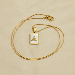 Détail macro d'un pendentif carré doré avec lettre A sur nacre et chaîne serpent