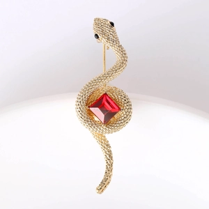 Macro detail of golden snake brooch featuring a large red gemstone and scale texture