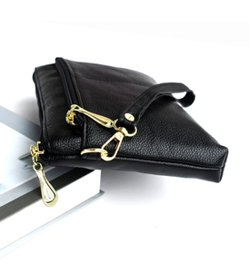 Detail of black lychee grain crossbody bag with gold zippers on white books