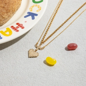 Close-up of double-layered gold necklace featuring a diamond heart and cross pendant