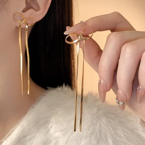 Gros plan de boucles d'oreilles nœud à pampilles dorées au style minimaliste chic