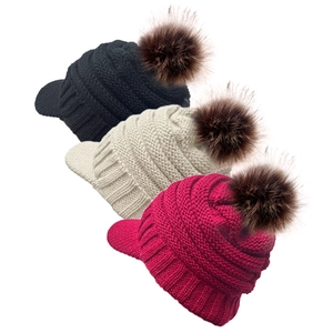 Detailed view of knitted winter hats with peaks and large brown faux fur pom poms in three colors