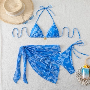 Three-piece bikini set with blue hibiscus print, sarong, and petal buckle on towel background