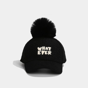 Detail einer schwarzen Lammwoll-Basecap mit flauschigem Bommel und WHAT EVER Stickerei