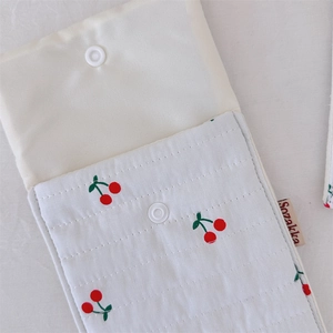 Close-up of quilted cherry print toiletry bag featuring white snap button and brand label