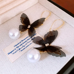 Detailed close-up of lace butterfly earrings with rhinestones and large faux pearls