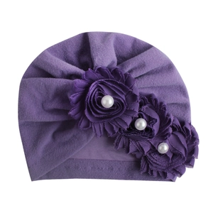 Detail der lila gefalteten Baby-Turban-Mütze mit drei Stoffblumen und künstlichen Perlen