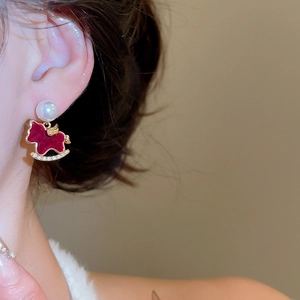 Close-up of model wearing red rocking horse earrings with pearls and gold details
