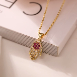 Detailed close-up of a gold Hamsa hand pendant necklace with red zircon flower inlay