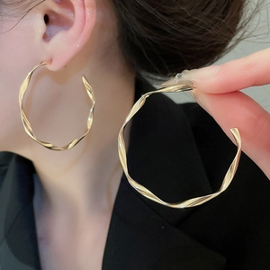 Detail of large golden twisted hoop earrings on model featuring a polished metal finish