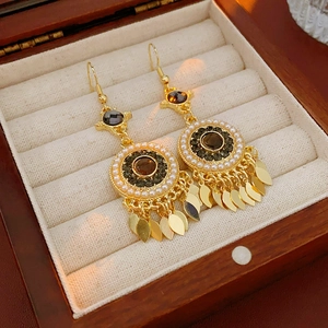 Gros plan de boucles d'oreilles bohèmes avec pampilles dorées, perles et pierres sombres