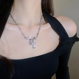 Detailed view of silver zircon cross necklace with safety pin pendant on model neck