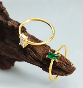 Detailopname van vergulde ringen met rechthoekige witte en groene stenen op hout