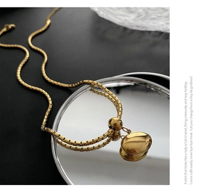 Detail of polished gold pebble pendant on a box chain reflecting on a mirror