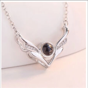 Macro detail of silver V-shaped wing necklace pendant with tiny crystals and round black stone