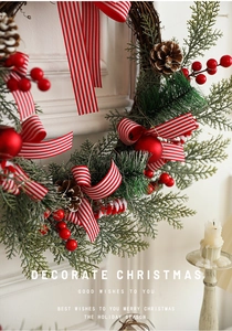 Detail of Christmas wreath with red berries, pine cones and striped bow on a white wall
