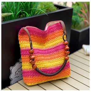 Detail of rainbow striped straw bucket bag with wood bead handle on a wooden surface