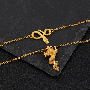 Detailed view of two gold snake pendants and caduceus necklace on a black slate background
