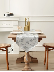 Detail of grey and black jacquard table runner with decorative tassel on wooden dining table