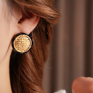Close-up of elegant gold textured round earrings with black enamel border worn by a model