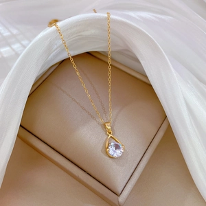 Close-up of gold water drop necklace with sparkling zircon on a beige gift box