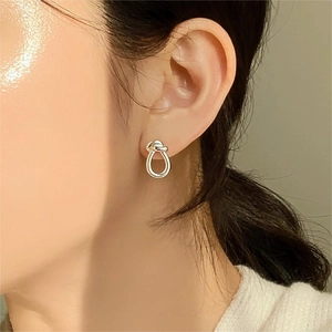 Close-up of polished 925 sterling silver knot stud earrings worn by a model