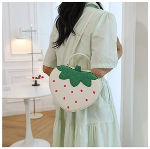 Rear view of a strawberry shaped crossbody bag in white and green on a model
